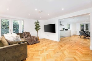 A modern living room with a sofa, a TV, and a dining area with chairs. - Designer 4-Bed, Skyline Views & Free Parking (London)