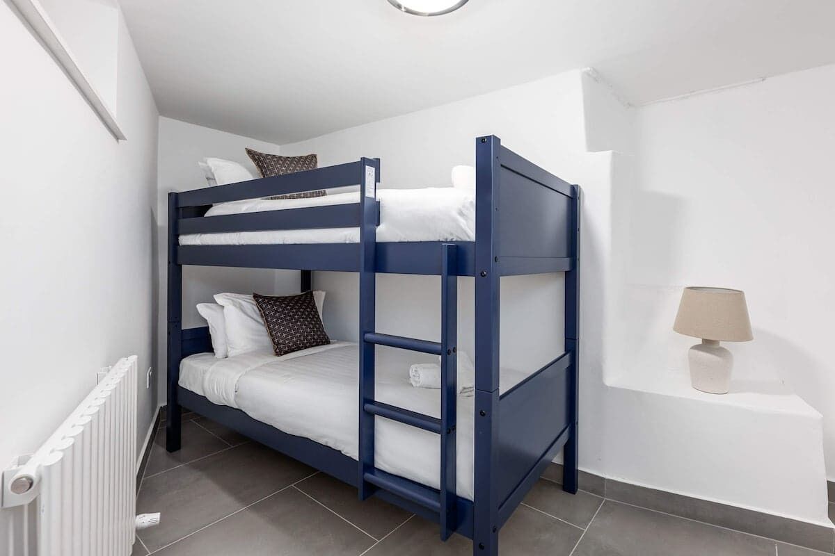 A bunk bed with white bedding, a lamp on a bedside table, and a radiator on the wall.