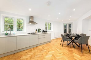 A modern kitchen with white cabinets, a herringbone wood floor, and a dining area with grey chairs. - Designer 4-Bed, Skyline Views & Free Parking (London)