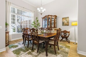 Ein Esszimmer mit einem Holztisch, sechs Stühlen, einer Chandelier, einem Schrank und einer Stehlampe.