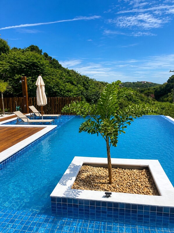 Ein Schwimmbecken mit Liegestühlen und einem Sonnenschirm, umgeben von einer Holzterrasse und einem Zaun.