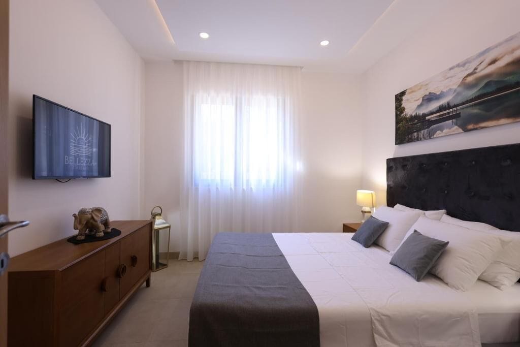 A bedroom with a bed, a TV, a painting, a nightstand, and a dresser.