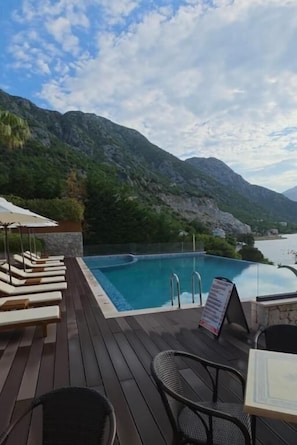 A wooden deck with lounge chairs, a pool, and a mountain backdrop.