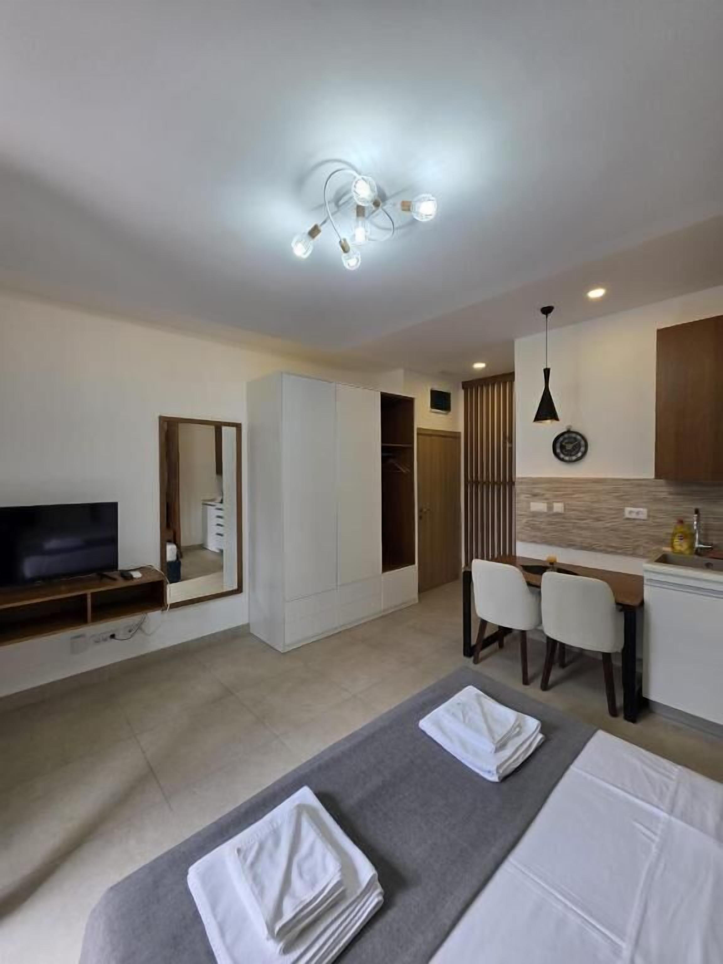Una habitación de hotel moderna con cama, televisión, escritorio con sillas y kitchenette.