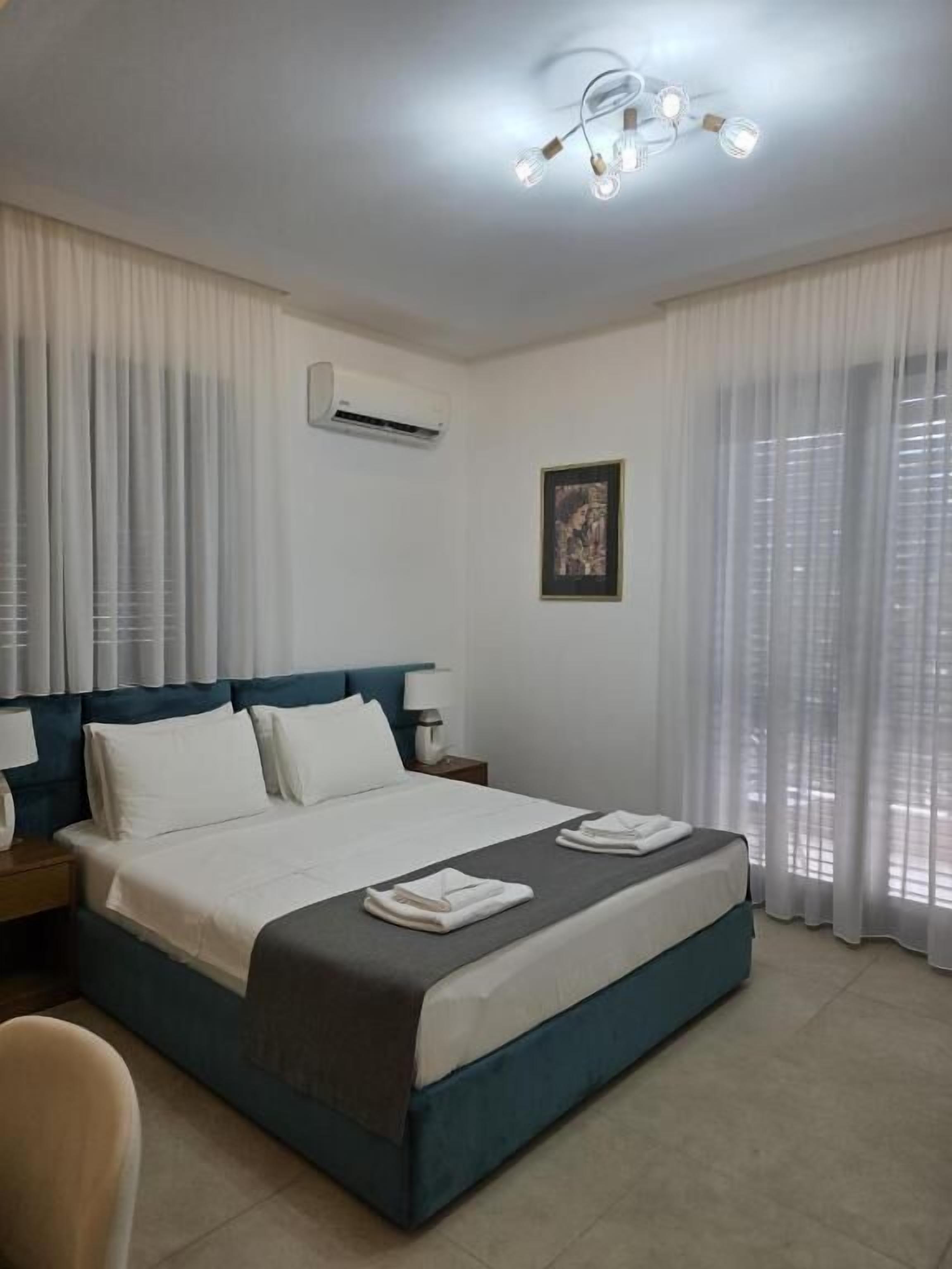 A hotel room with a bed, curtains, an air conditioning unit, a framed picture, and a ceiling light fixture.