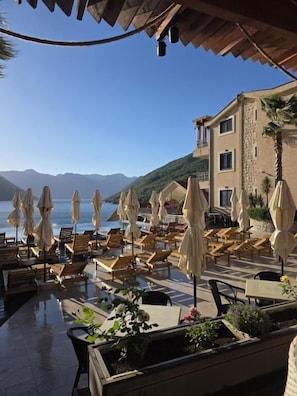 A terrace with lounge chairs and umbrellas, overlooking a body of water and mountains. - Bellezza Condo Apartments (Morinj)