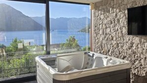 A modern bathroom with a large bathtub, a stone wall, and a view of a lake and mountains. - Bellezza Residence & Spa Kotor (Kotor)