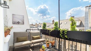 En balkon med en sofa, et lille bord med blomsterpotter og udsigt over bybilledet.