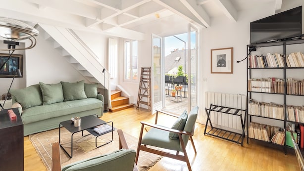 En moderne stue med en grøn sofa, et sofabord, en bogreol og en trappe til et udendørs område.