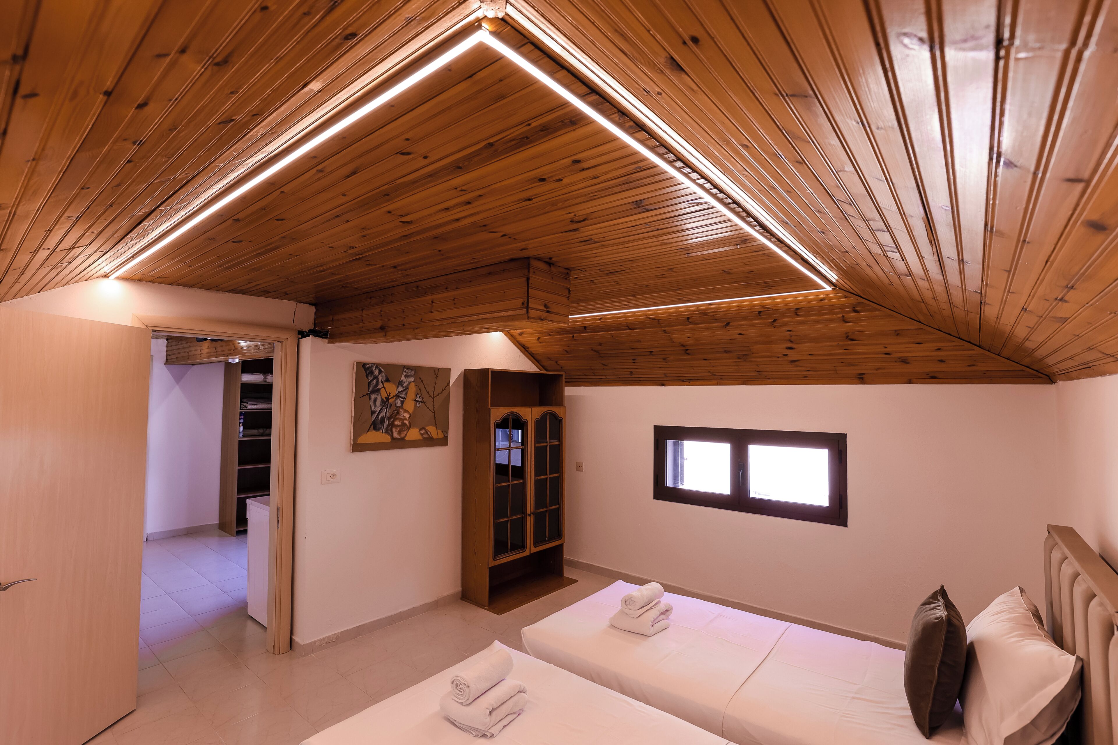 Une pièce avec des poutres apparentes en bois au plafond, deux lits avec des serviettes, une fenêtre et une porte donnant sur une autre pièce.