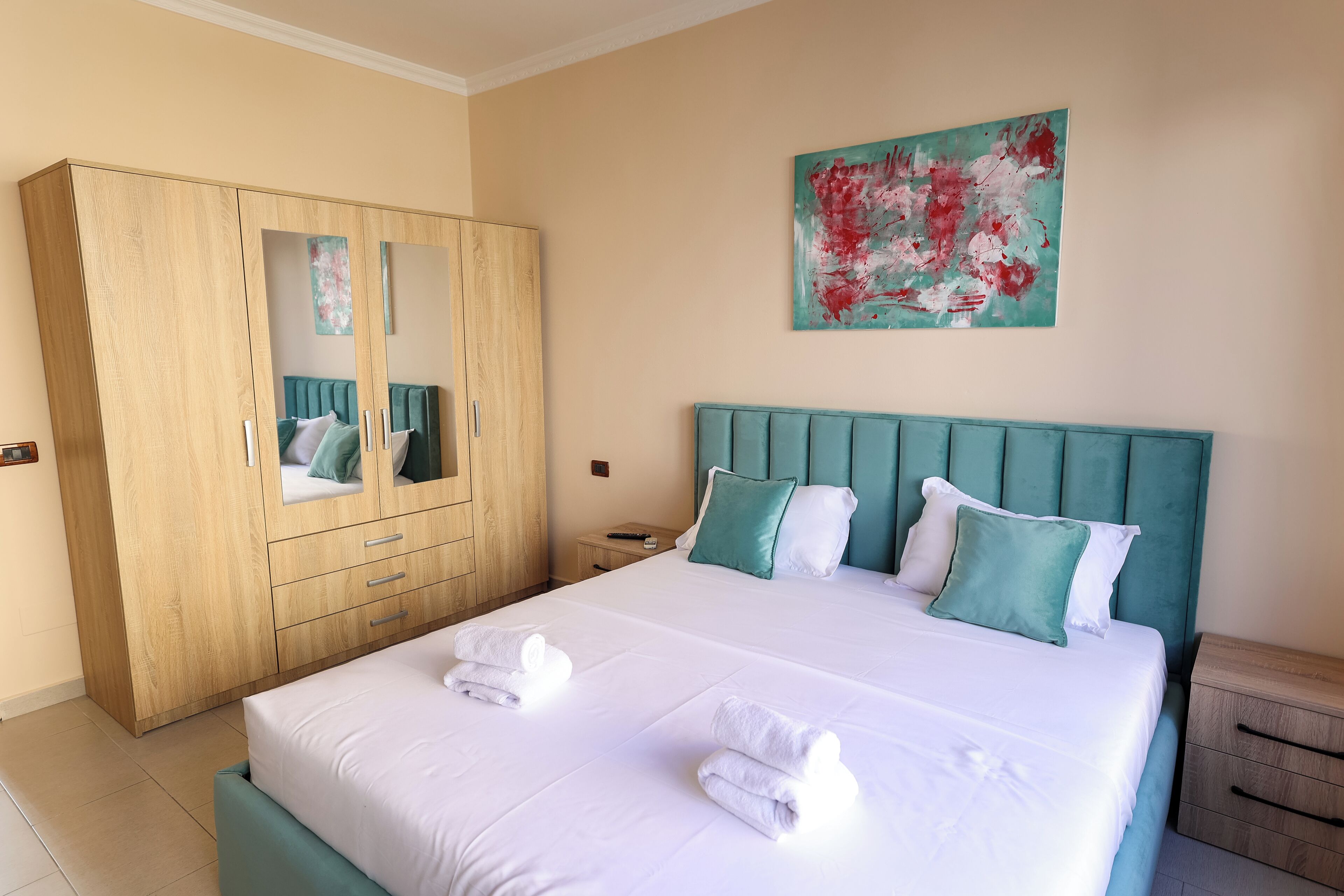 A hotel room with a large bed, a wardrobe, a nightstand, and a painting on the wall.