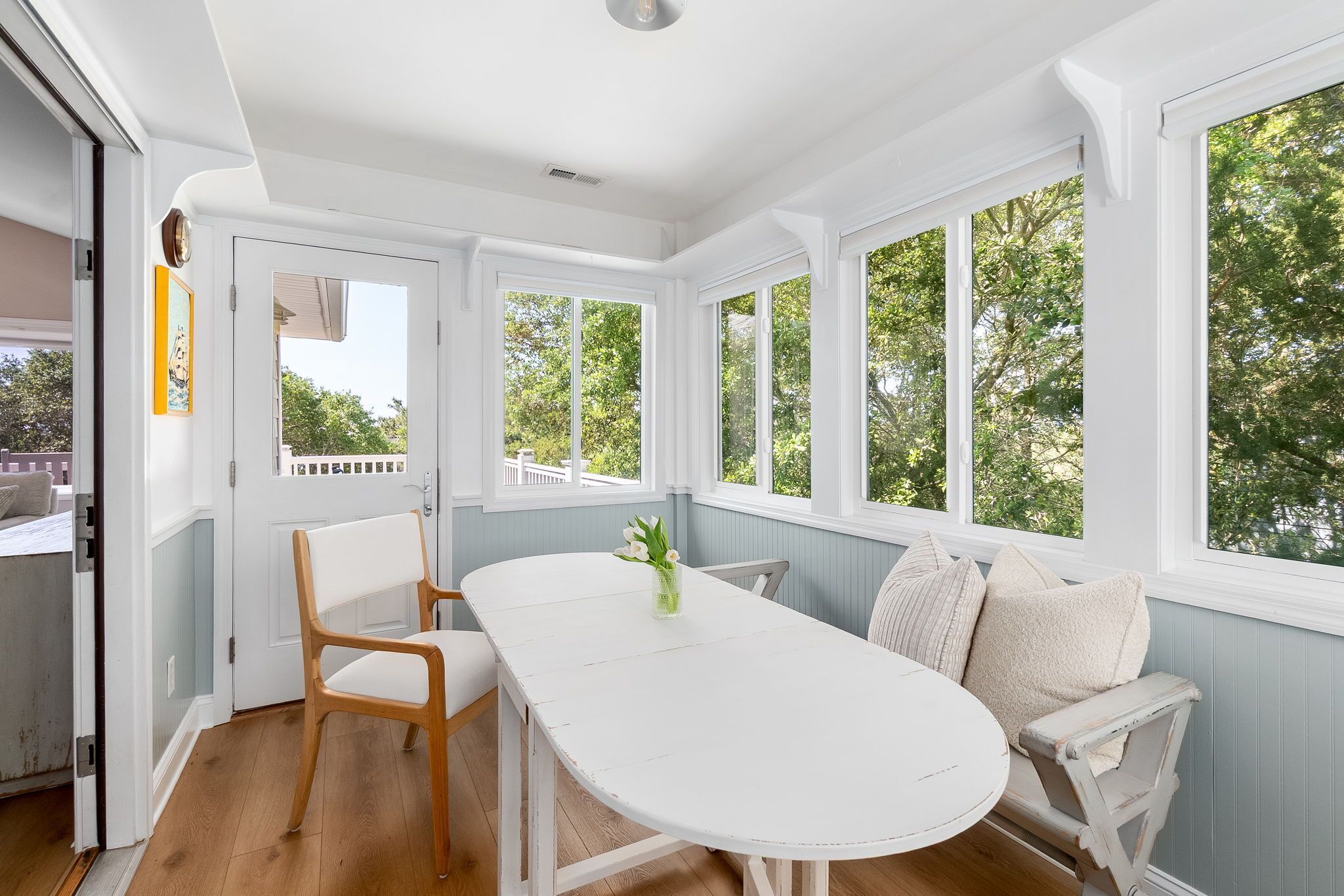 A room with a white table, a white bench, and large windows with a view of trees.
