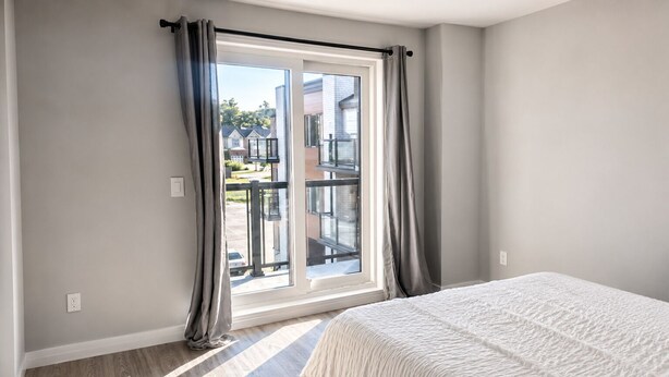 Un dormitorio con una ventana grande, una cama y vista a una zona residencial.