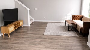 Una sala de estar con un televisor de pantalla plana sobre un soporte de madera, un sofá de cuero marrón, una mesa de centro y una alfombra estampada.