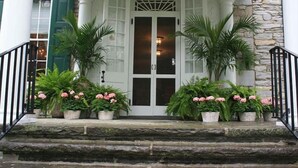 Una entrada principal con puerta blanca, escalones de piedra y plantas en macetas.