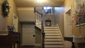 Un escalier avec une rampe, une porte, un luminaire fixé au mur et une petite table sur laquelle se trouve un vase.