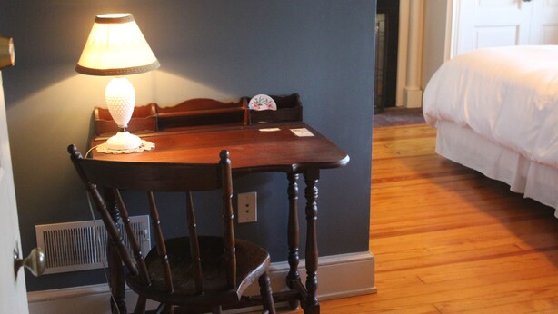 Una habitación con una mesa de madera, una silla, una lámpara, una cama y una puerta.