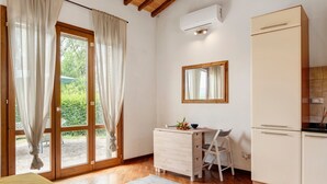 Une pièce avec un plancher en bois, un lit, un bureau avec une chaise, une petite table avec un bol et des fleurs, un miroir et une armoire blanche.