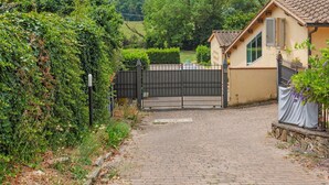 Une allée pavée mène à une entrée fermée par un portail, avec une maison en arrière-plan.