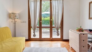 Une pièce avec un plancher en bois, une chaise jaune, un bureau blanc avec des tiroirs, un miroir et une porte avec des rideaux.