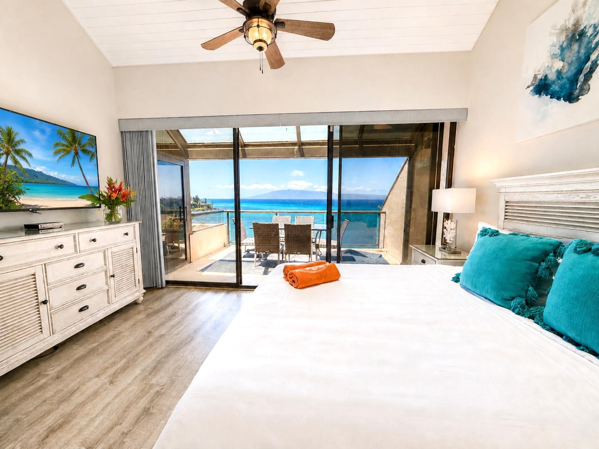 Een hotelkamer met een groot bed, een plafondventilator, een televisie, een bureau en uitzicht op de oceaan.
