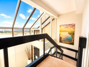 Ein modernes Interieur mit einer Glasstufen-Wendeltreppe, einem Sonnenuntergangsgemälde und Blick auf die Stadtlandschaft.
