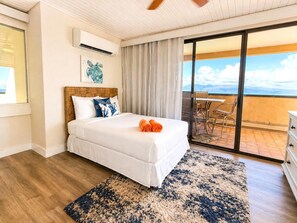 Ein Hotelzimmer mit Bett, großem Fenster, Klimaanlage, Deckenventilator, Balkon mit Tisch und Stühlen und Blick zum Himmel.