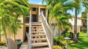 A two-story building with a wooden staircase leading to a door, surrounded by palm trees and greenery. - Kuilima Estates 2 Golf View Villas, Sleeps 16 | Car Incl. w/ 6 Nights | KUL ML-4046 by KBM (Kahuku)
