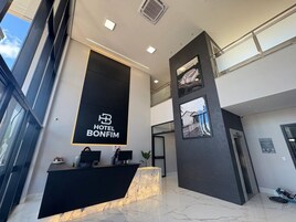 Un vestíbulo de hotel moderno con una mesa de recepción, un gran letrero negro con el nombre del hotel y una escalera que conduce al piso superior.
