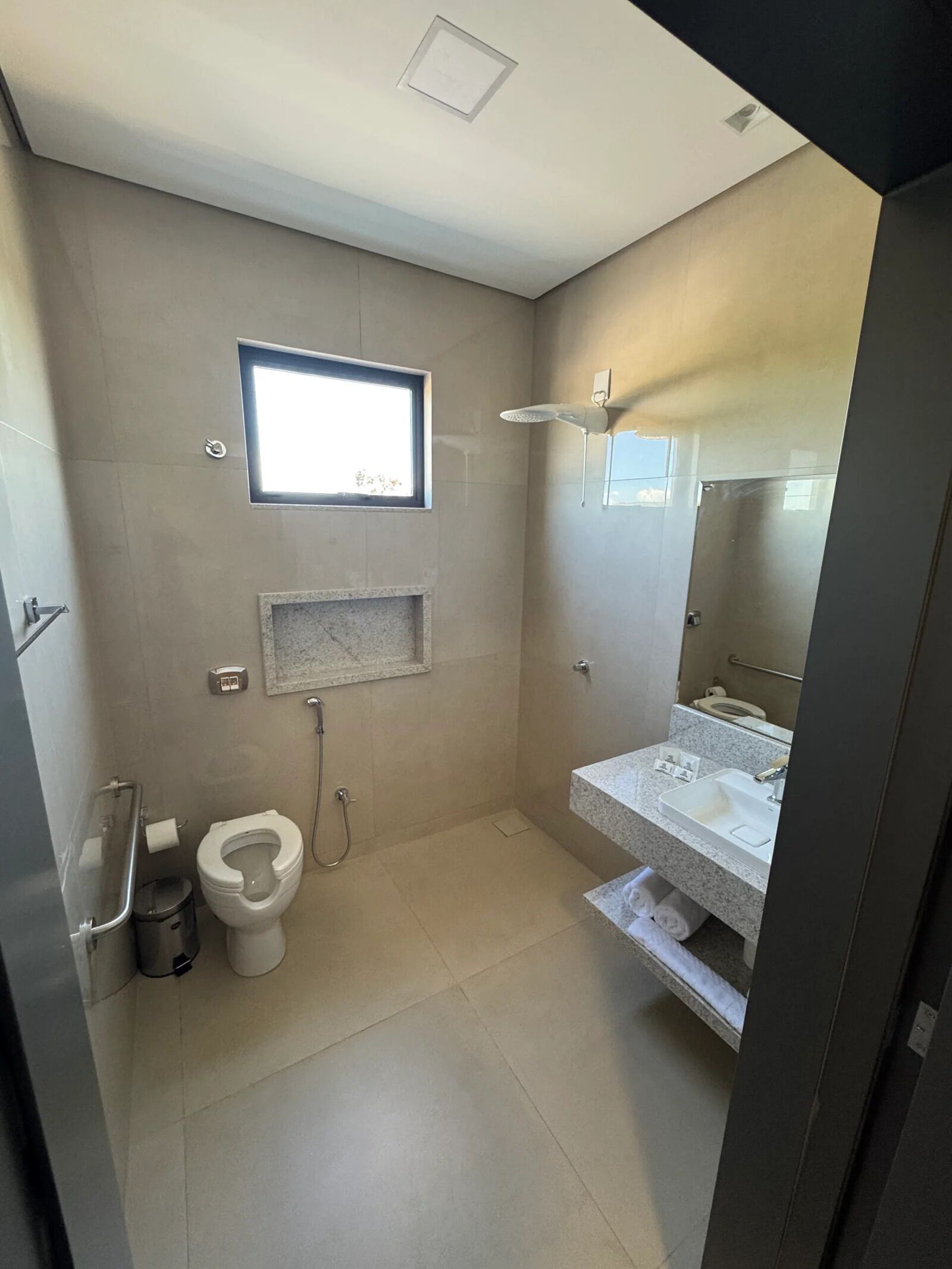 A modern bathroom with a toilet, shower, sink, and a small window.
