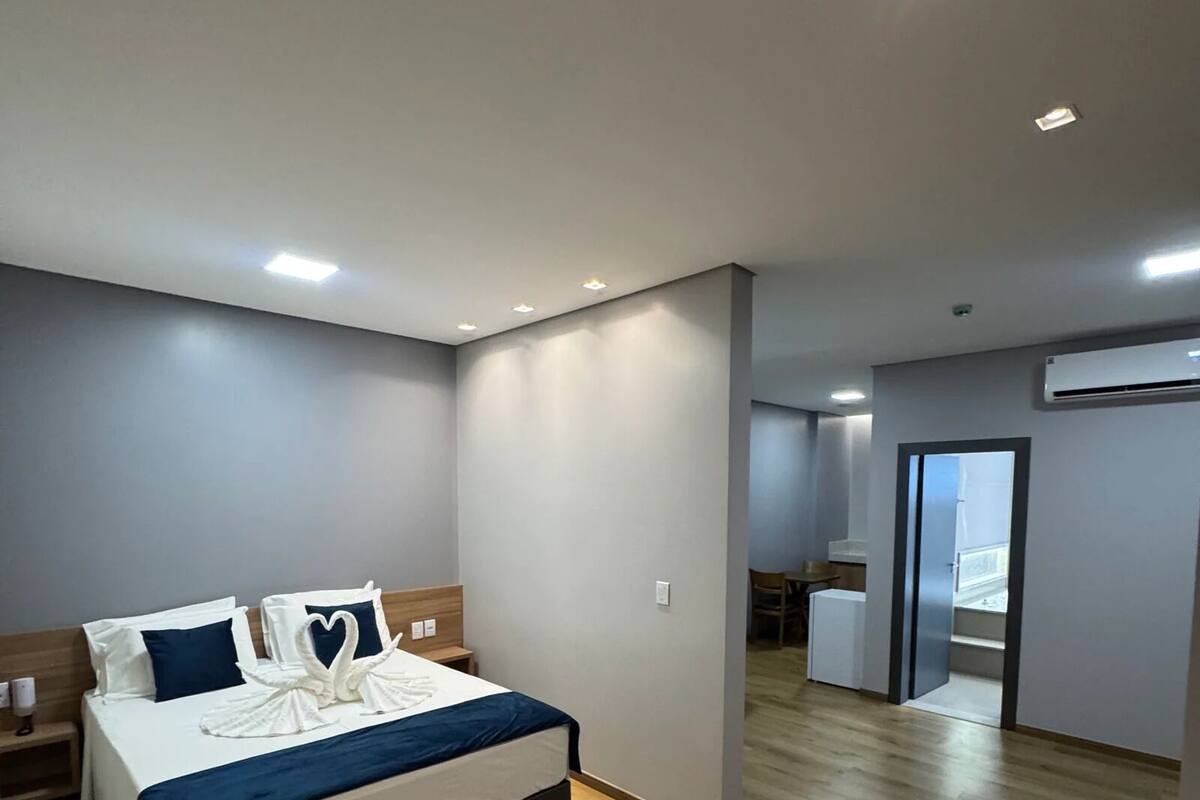 Una habitación de hotel moderna con una cama grande, mesitas de noche, un armario y un baño visible a través de una puerta abierta.