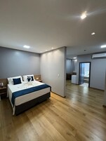 Una habitación de hotel moderna con una cama grande, mesitas de noche, un armario y un baño visible a través de una puerta abierta.