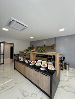 Una habitación de hotel moderna con piso de mármol, una isla central con alimentos para el desayuno, un mueble de madera y un cartel que dice 'SALIDA'.