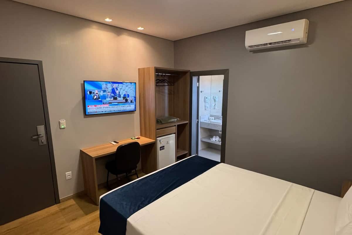Una habitación de hotel con cama, escritorio, televisor y aire acondicionado.