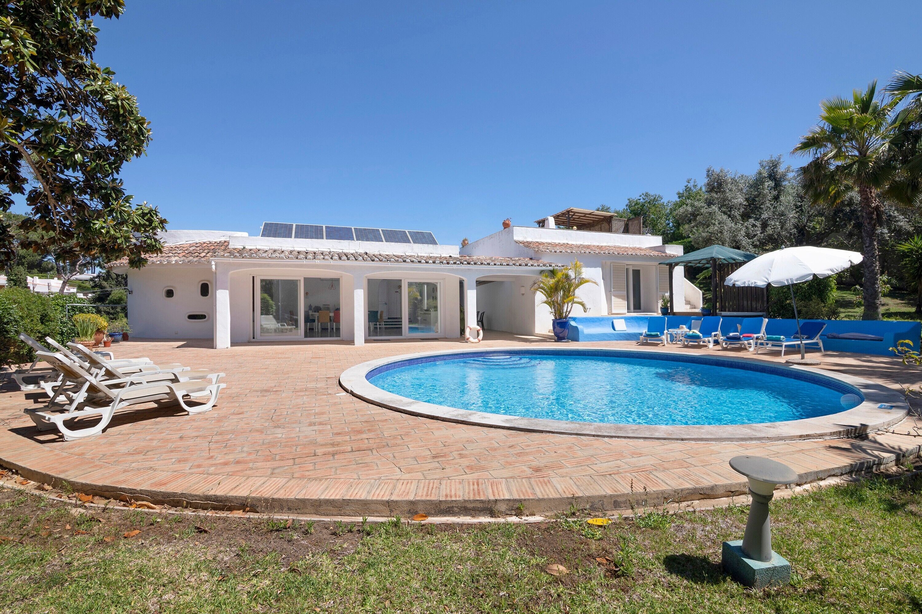 Una piscina con sillas de descanso, un patio cubierto y una casa con paneles solares.
