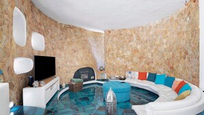 Une salle de spa avec un mur en pierre, un téléviseur à écran plat, une cheminée, un canapé blanc incurvé agrémenté de coussins colorés et une petite tour décorative.