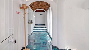 Un couloir avec un sol carrelé, des murs blancs, un plafond en briques et un chapeau accroché au mur.