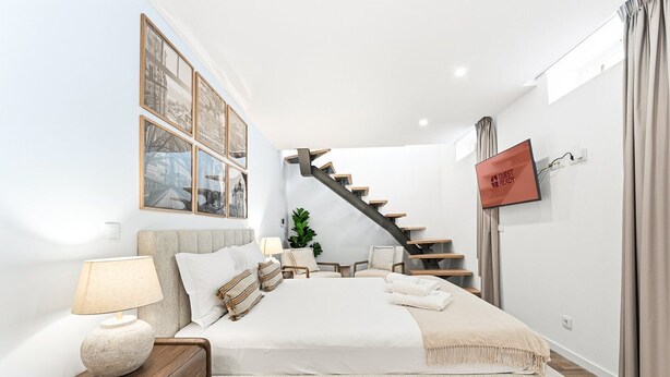A bedroom with a bed, nightstand, lamp, framed pictures, a staircase, and a sign. - GuestReady - Charming stay in Porto (Porto)
