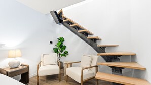 A modern interior with a wooden staircase, two white armchairs, a small table with a lamp, and a potted plant. - GuestReady - Charming stay in Porto (Porto)