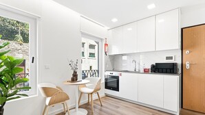 A compact kitchen with white cabinets, a microwave, and an oven. There is a dining area with two chairs and a table. - GuestReady - Charming stay in Porto (Porto)