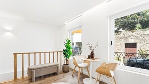 A room with a wooden bench, a potted plant, a round table with chairs, and a view of a stone wall outside. - GuestReady - Charming stay in Porto (Porto)