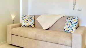 A beige sofa with patterned pillows, a white wall with framed pictures, and a telephone. - La terrazza sul blu - Marina di Ragusa (Marina di Ragusa)