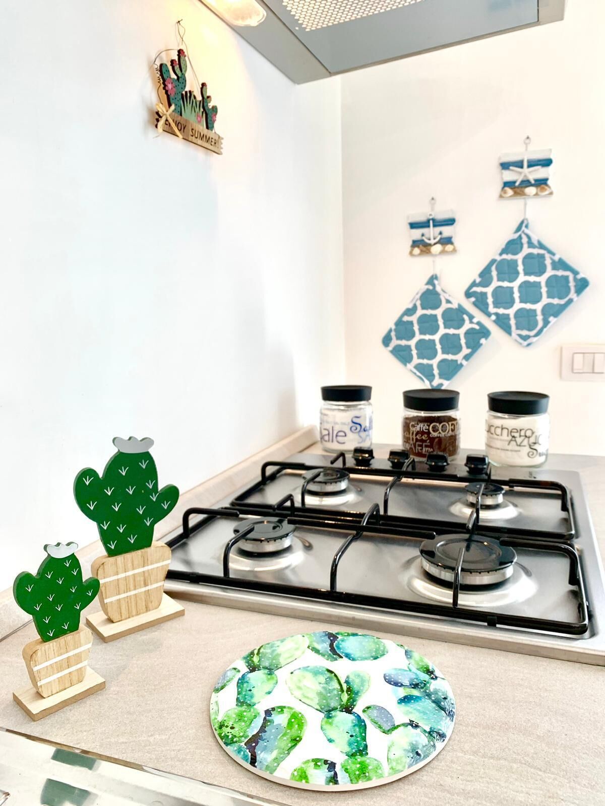 A kitchen with a gas stove, wooden cactus decorations, a plate with cactus pattern, and kitchen utensils on the wall.