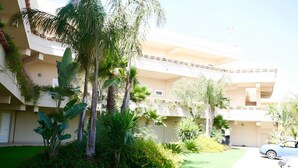 A multi-story building with balconies, surrounded by lush greenery and palm trees. - La terrazza sul blu - Marina di Ragusa (Marina di Ragusa)