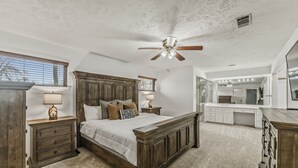 A bedroom with a large bed, a ceiling fan, a nightstand with a lamp, and a dresser. - Hoofs and Horns Private Ranch (Huntsville)