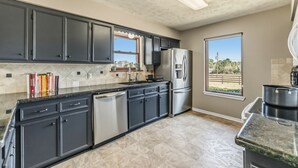 A kitchen with dark cabinets, a stainless steel refrigerator, and a window with a view of greenery. - Hoofs and Horns Private Ranch (Huntsville)