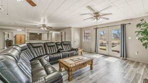 A spacious living room with a leather sectional sofa, a wooden coffee table, and two ceiling fans. - Hoofs and Horns Private Ranch (Huntsville)