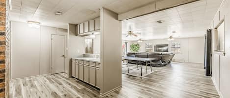 Una cocina moderna con una isla central, un comedor con mesa y sillas, y una sala de estar con sofá y televisor.