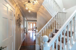 A hallway with white doors, a staircase with white balusters, and a ceiling light fixture.
