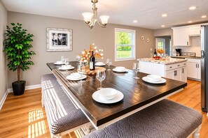 A modern kitchen with white cabinets, a wooden island, and a dining area with a large table set for six. - Hot Tub • Game Room • 5BR • Suburb near Everything (Rochester)